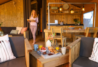 Frau serviert Frühstück in einem komfortablen Glamping-Zelt mit Holzmöbeln im Ferienpark.