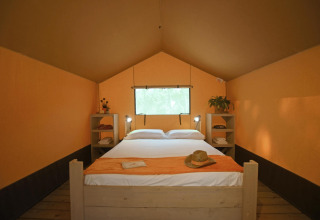 Vista interior de la tienda Safari tent Cozy con cama doble en TinyParks Cast Away, Países Bajos, con desayuno.