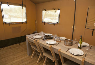 Interieur van een luxe safaritent met gedekte eettafel bij vakantiepark De Boshoek in Nederland.