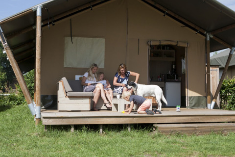Familie mit Hund entspannt vor einem Luxus-Safari-Zelt im Holidaypark De Boshoek, Niederlande.