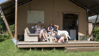 Famiglia con cane si rilassa davanti a una tenda safari di lusso al Holiday park De Boshoek, Olanda.