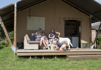 Familie mit Hund entspannt vor einem Luxus-Safari-Zelt im Holidaypark De Boshoek, Niederlande.