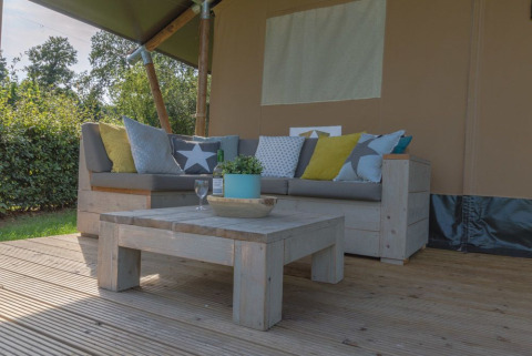 Udendørs siddeområde med sofa, sofabord og puder ved luksus safari telt i Holiday park De Boshoek, Holland.