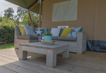 Buiten zithoek met bank, salontafel en kussens bij de luxe safaritent op Vakantiepark De Boshoek, Nederland.