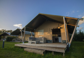 Tienda safari en Holiday park De Boshoek, Países Bajos, con terraza de madera y asientos en el exterior.
