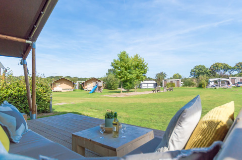 Vista desde la terraza de una tienda safari en Holiday park De Boshoek, Países Bajos, con césped y parque infantil.