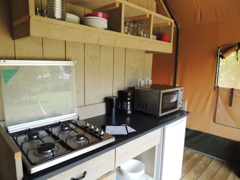 Küchenbereich im Safarizelt im Holiday Park De Boshoek, mit Gasherd, Mikrowelle und Geschirr.