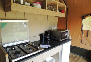 Coin cuisine d’une tente safari à Holiday park De Boshoek avec gazinière, micro-ondes et vaisselle.