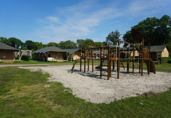 Playground with climbing equipment in front of several safari tents at a campsite under a blue sky.