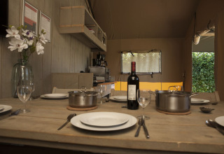 Mesa de comedor en una tienda safari en Holiday park De Boshoek, Países Bajos, con platos, ollas y vino.