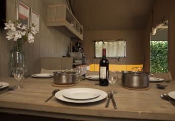 Dining table set inside a safari tent at Holiday park De Boshoek, Netherlands, with plates, pots, and wine.