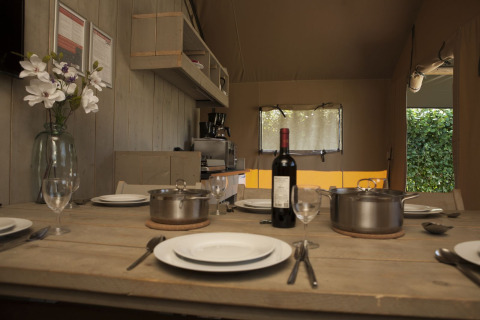 Dining table set inside a safari tent at Holiday park De Boshoek, Netherlands, with plates, pots, and wine.