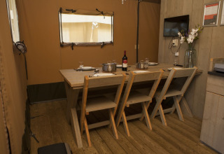 Zona de comedor en tienda safari en Holiday park De Boshoek, Países Bajos, mesa y sillas de madera.