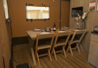 Dining area inside a safari tent at Holiday park De Boshoek, Netherlands, with four wooden chairs and table.