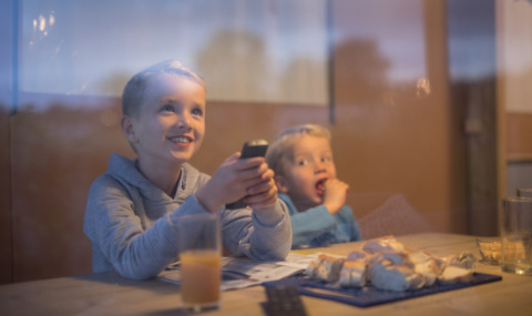 Two kids enjoy snacks and juice while watching TV in a luxury safari lodge at De Boshoek, Netherlands.