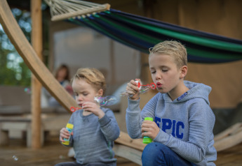 To børn blæser sæbebobler foran en luksus safarilodge i ferieparken De Boshoek i Holland.