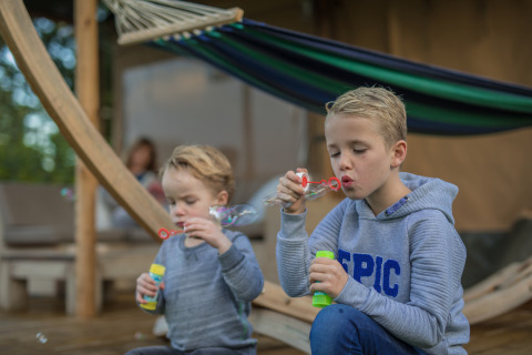 Twee kinderen blazen zeepbellen bij een luxe safarilodge in vakantiepark De Boshoek, Nederland.