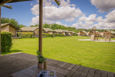 Vista da una tenda safari lodge di lusso al Holiday park De Boshoek, Paesi Bassi, con prato e area giochi.