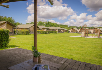 Uitzicht vanuit een luxe safarilodgetent op Holiday park De Boshoek, Nederland, met grasveld en speeltuin.