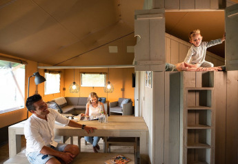 Famiglia che si gode una tenda Safari House al parco vacanze De Boshoek, Paesi Bassi, bambino nel soppalco.