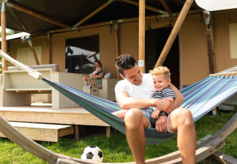 Padre e figlio si rilassano su un'amaca davanti a una tenda safari al parco De Boshoek, Paesi Bassi.