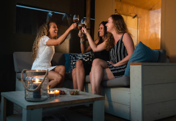 Tre kvinder skåler med vin på en hyggelig terrasse i Safari House, feriepark De Boshoek, Holland.