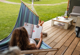 Vrouw leest een tijdschrift in een hangmat op het terras van Safari House, park De Boshoek, Nederland.