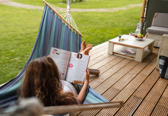 Mujer leyendo una revista en una hamaca en la terraza de Safari House, parque De Boshoek, Países Bajos.