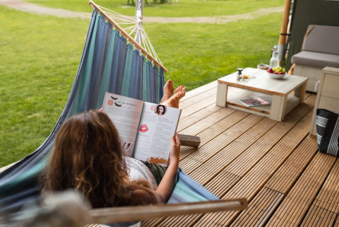 Frau liest ein Magazin in einer Hängematte auf der Terrasse des Safari House im Ferienpark De Boshoek.