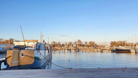 Casa flotante De Zwerver en Marina Parcs Naarden, Países Bajos, atracada en el puerto bajo cielo despejado.