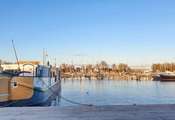 Hausboot De Zwerver im Marina Parcs Naarden in den Niederlanden, vertäut im Yachthafen bei klarem Himmel.