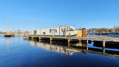 La casa flotante De Zwerver amarrada en Marina Parcs Naarden, Países Bajos, bajo el cielo despejado.
