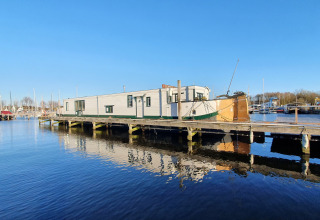 Woonboot De Zwerver ligt aangemeerd bij Marina Parcs Naarden in Nederland, weerspiegeld in het water.