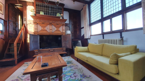 Salon de la péniche De Zwerver avec canapé jaune, meubles en bois et grandes fenêtres à Naarden, Pays-Bas.