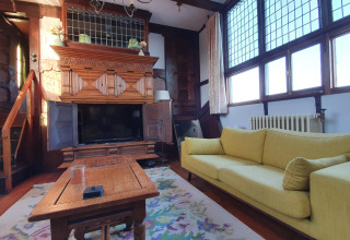 Salon de la péniche De Zwerver avec canapé jaune, meubles en bois et grandes fenêtres à Naarden, Pays-Bas.