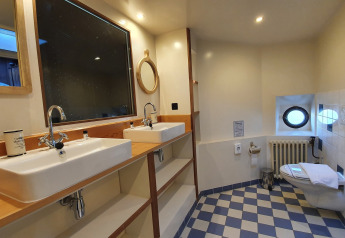 Baño con doble lavabo, espejos y aseo en el Houseboat De Zwerver en Marina Parcs Naarden, Países Bajos.