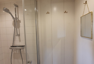 Shower with white tiled walls, hooks, and a mirror inside Houseboat De Zwerver at Marina Parcs Naarden.