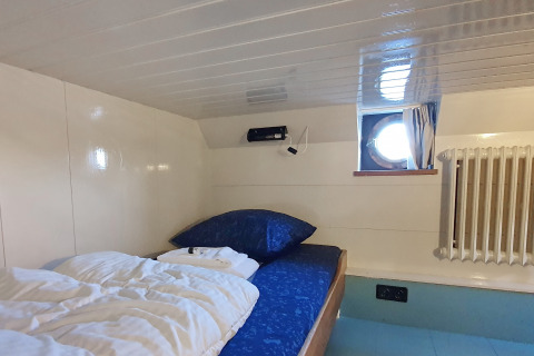 Cabine confortable avec lit simple, hublot et radiateur sur la Houseboat De Zwerver à Naarden, Pays-Bas.