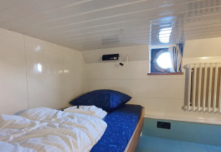 Kleines gemütliches Schlafzimmer mit Einzelbett, Bullauge und Heizung auf Houseboat De Zwerver in Holland.