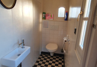 Schmales Badezimmer auf einem Hausboot mit Schachbrettboden, WC, kleinem Waschbecken und Fenster.