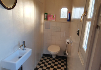 Schmales Badezimmer auf einem Hausboot mit Schachbrettboden, WC, kleinem Waschbecken und Fenster.