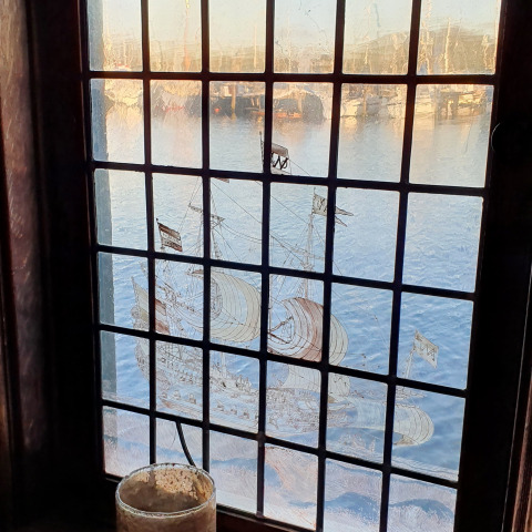 Zicht door een glas-in-loodraam in houseboat De Zwerver met schip bij Marina Parcs Naarden, Nederland.