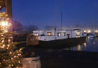 Abendaufnahme vom Hausboot De Zwerver im Marina Parcs Naarden, mit beleuchtetem Baum und Booten.