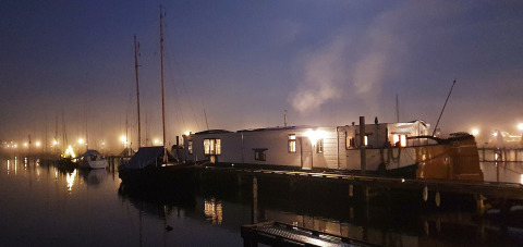 Atmospheric evening photo of Houseboat De Zwerver at Marina Parcs Naarden in the Netherlands, lights aglow.
