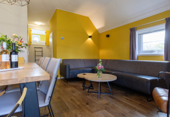 Salon moderne à Vechtdallodge, Kampeerdorp de Zandstuve, Pays-Bas, avec murs jaunes et canapé d’angle.