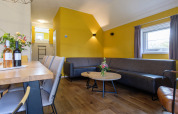 Modernes Wohnzimmer in der Vechtdallodge im Kampeerdorp de Zandstuve, Niederlande, mit gelber Wand und Sofa.