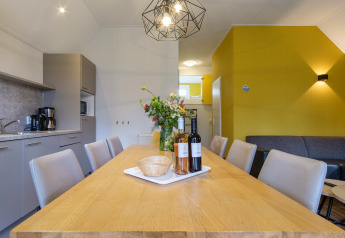 Salle à manger moderne à Vechtdallodge, Kampeerdorp de Zandstuve, Pays-Bas, avec table en bois et fleurs.