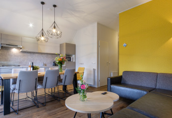 Modernes Wohnzimmer und Küche in der Vechtdallodge im Kampeerdorp de Zandstuve, Niederlande, mit gelber Wand.