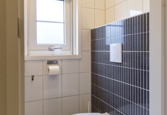 Et moderne toilet med hvidt sæde, grå fliser, vindue og udluftningsventil i Vechtdallodge, Nederlandene.