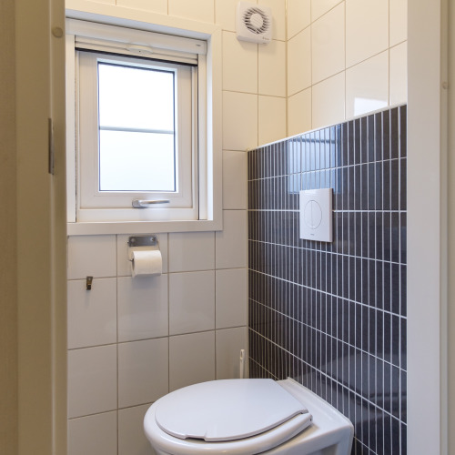 Baño moderno con inodoro, ventana, extractor y azulejos grises en Vechtdallodge, Países Bajos.